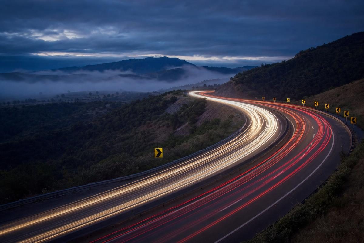 Highway curve at dusk with red and white light trails and chevron warning signs illustrating an accident probability calculator