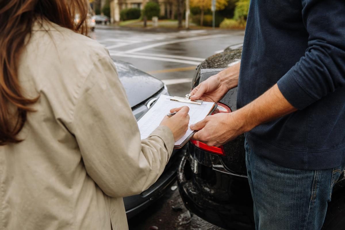 Two drivers exchange paperwork on a clipboard after a minor car accident settlement calculator fender bender at an intersection