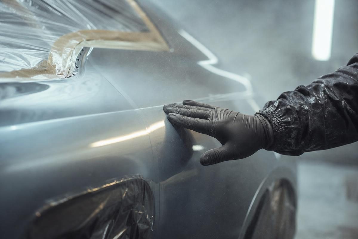 Gloved body shop hand checking a repaired mismatched fender panel for a car value after accident calculator